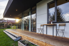 Drevená terasa lemujúca dom z dvoch strán je presahom strechy chránená pred slnkom a dažďom