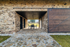 Voľný „prejazd“ domom slúži ako krytá terasa na vonkajšie posedenie. Z oboch strán ho možno uzavrieť posuvnými drevenými vrátami a vytvoriť plne chránený priestor