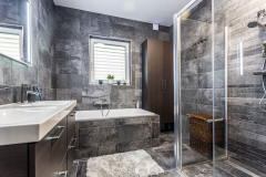 V kúpeľni použili mramorovo sivé obklady stien, podlahy i vane. Naproti dvojitému umývadlu sa nachádza minimalistický sprchový kút