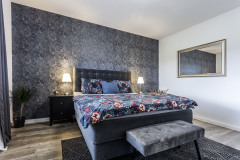 Interiér spálne skvele pracuje s farebnými kombináciami. Farba steny za čelom postele korešponduje s farbou postele, taburetu a kobercom