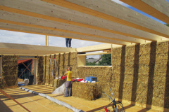 Stavba pasívneho domu. Obálku domu tvoria balíky, vyrobené priamo na poli. K pozitívnej energetickej bilancii prispieva aj presklená južná stena a vegetačná strecha