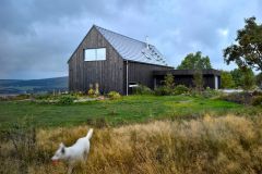 Garáž pre dva automobily je predsadená pred domom a zastrešená plochou strechou. Pozdĺž nej vedie prístup k hlavným vchodovým dverám, ktorý je prekrytý strieškou