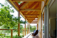 Krytá terasa pozdĺž celej južnej strany domu v prípade pekného počasia slúži ako „vonkajšia obývačka“. Okno na presahujúcej streche je poistkou proti nedostatku denného svetla tak na terase, ako aj v interiéri