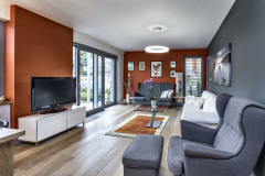 Spoločnú obývaciu časť domu tvorí priestor so sedením, jedálňou a kuchyňou. Jeho súčasťou je veľké akvárium, splnený sen domáceho pána. Majitelia majú radi prírodu, preto do obytných miestností zvolili lepenú drevenú dlážku vo vyhotovení patinovaný dub. Krásne s ňou ladí farebná kombinácia sivej, bielej a tehlovočervenej farby, ktorá pôsobí harmonicky a nie nudne