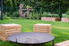 Od ohniska sa ponúka pohľad na kovovú sochu Jakuba Flejšara, ktorá nielen dotvára srdečnú atmosféru záhrady, ale navyše je aj funkčná: ponúka blízky zdroj dreva pre ohnisko